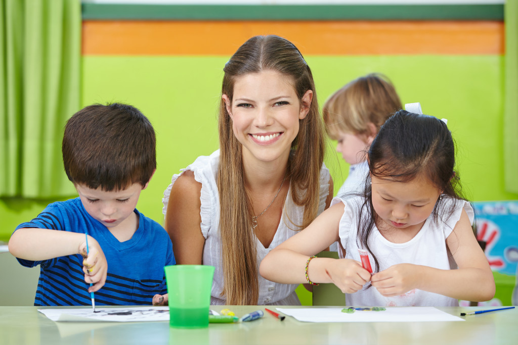A teacher smiling in class while her students are doing arts